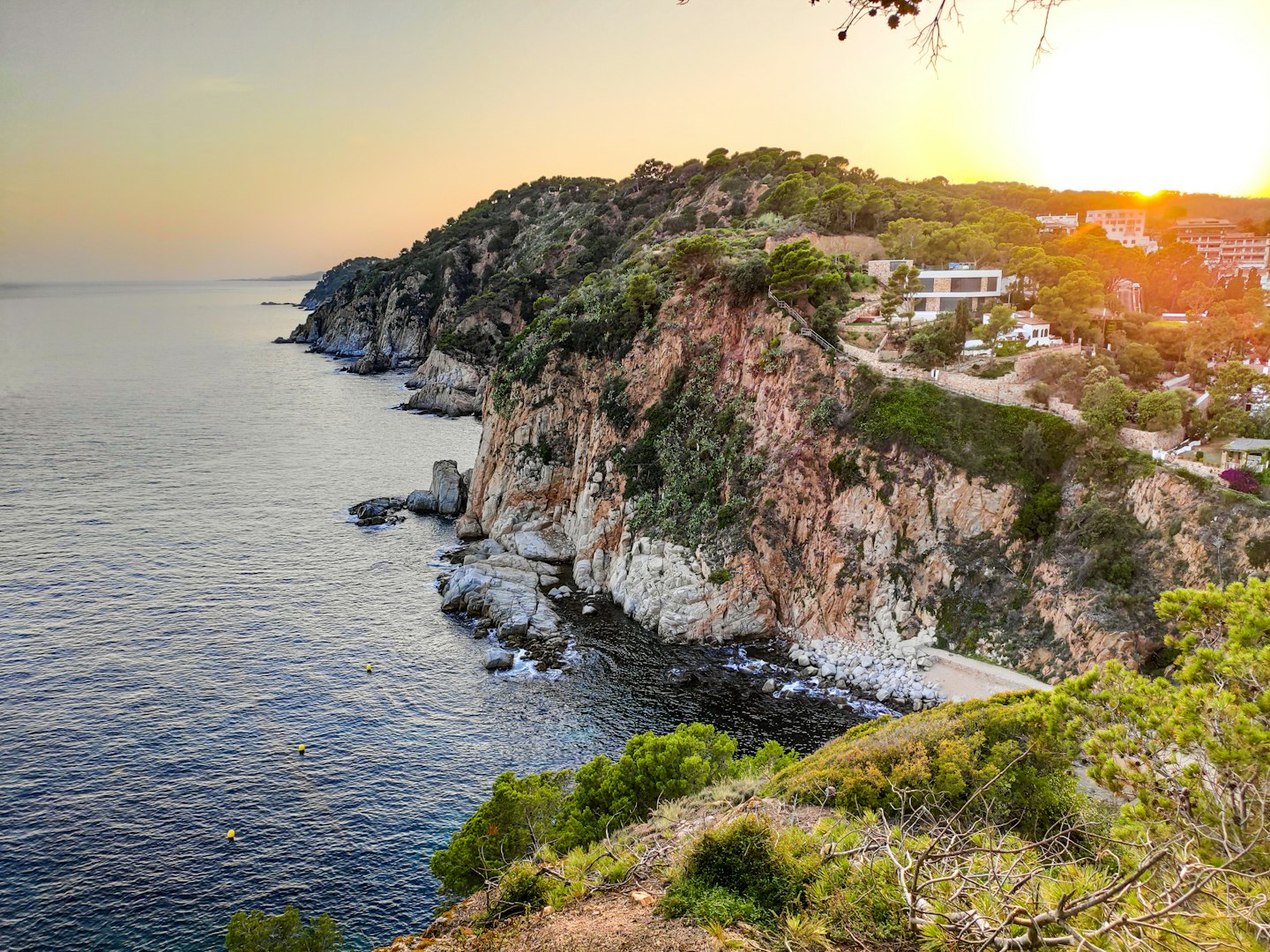 Scogliere della costa mediterranea al tramonto con mare ed edifici.