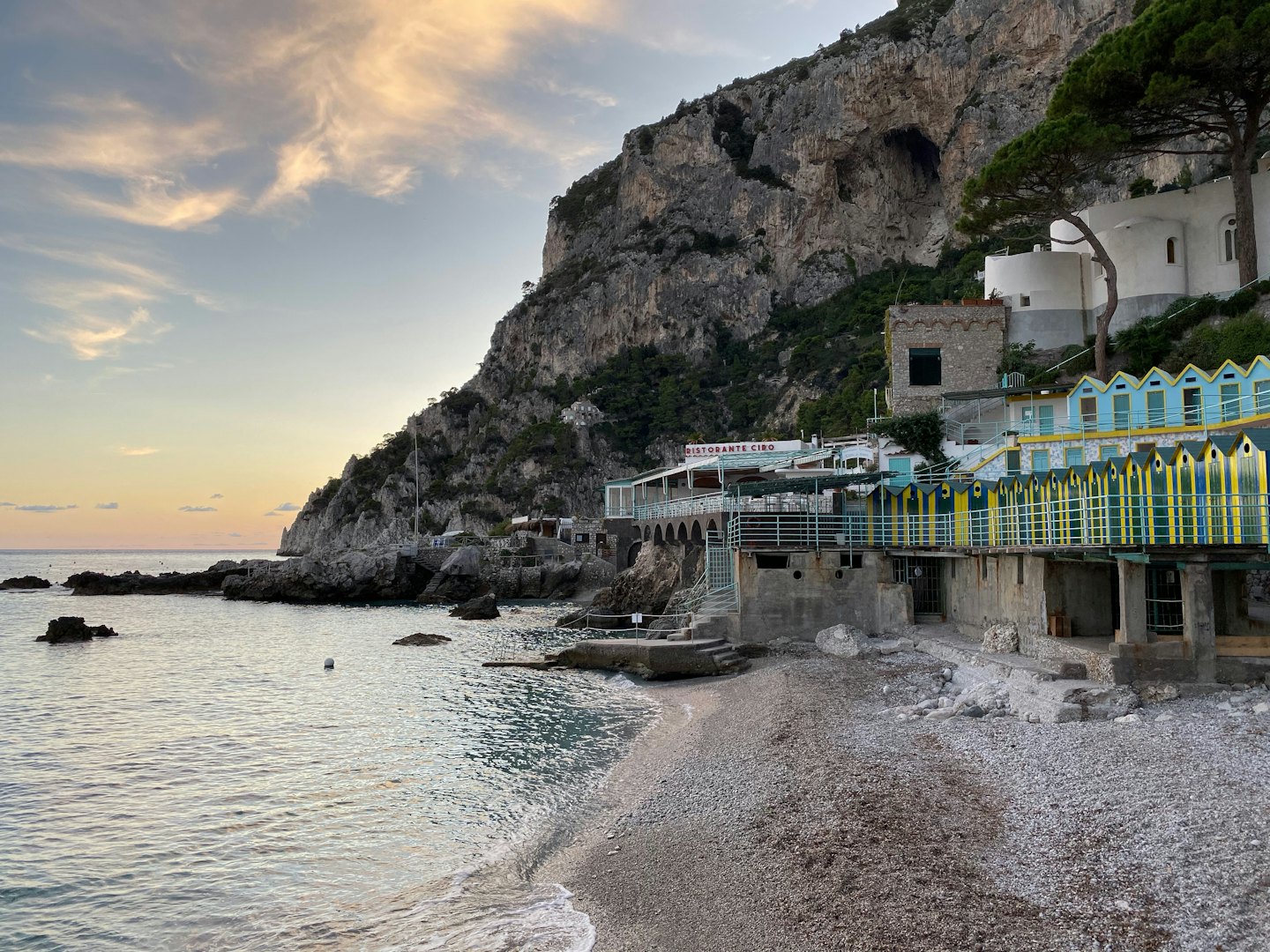 Villaggio costiero con cabine sulla spiaggia sotto ripide scogliere rocciose.