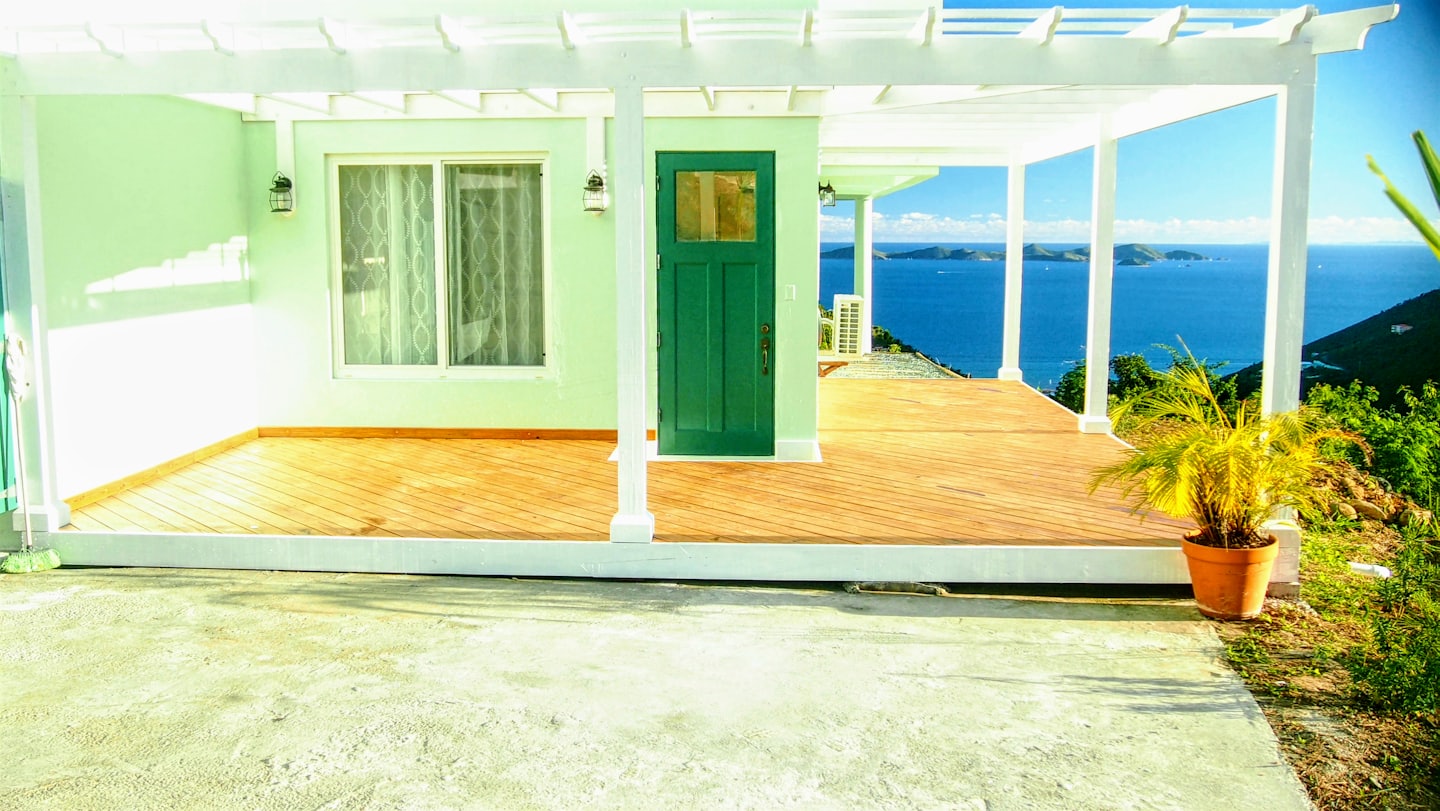 Casa verde chiaro con terrazza in legno affacciata sull'oceano blu.