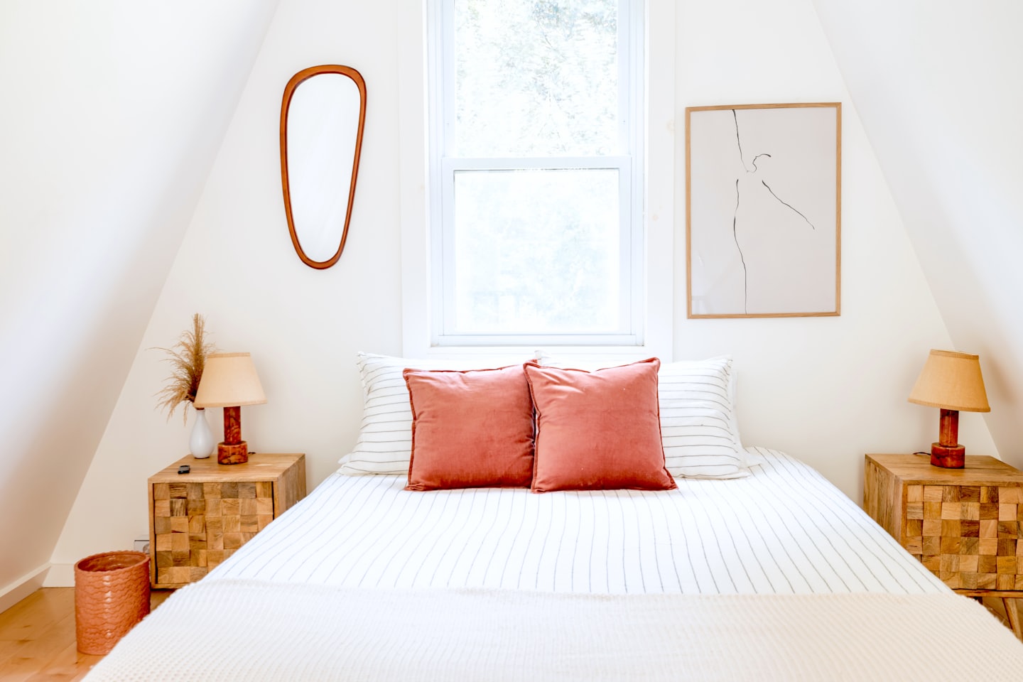 Camera da letto mansardata con biancheria da letto a righe e cuscini corallo.